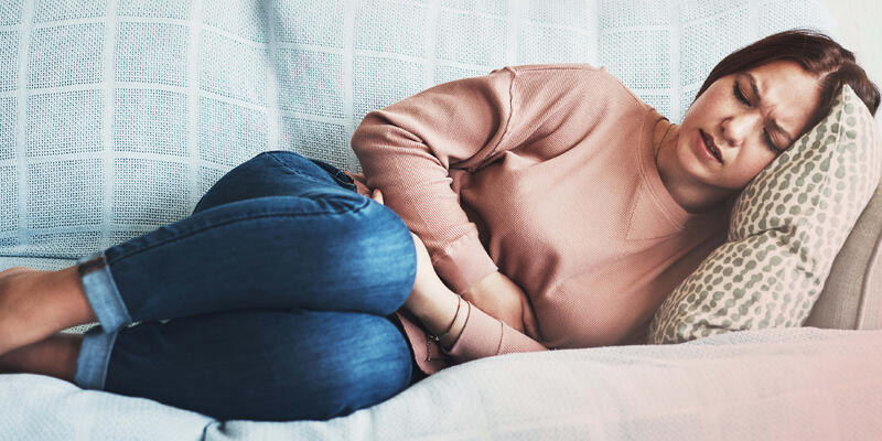 A woman laying on the couch holding her stomach in pains